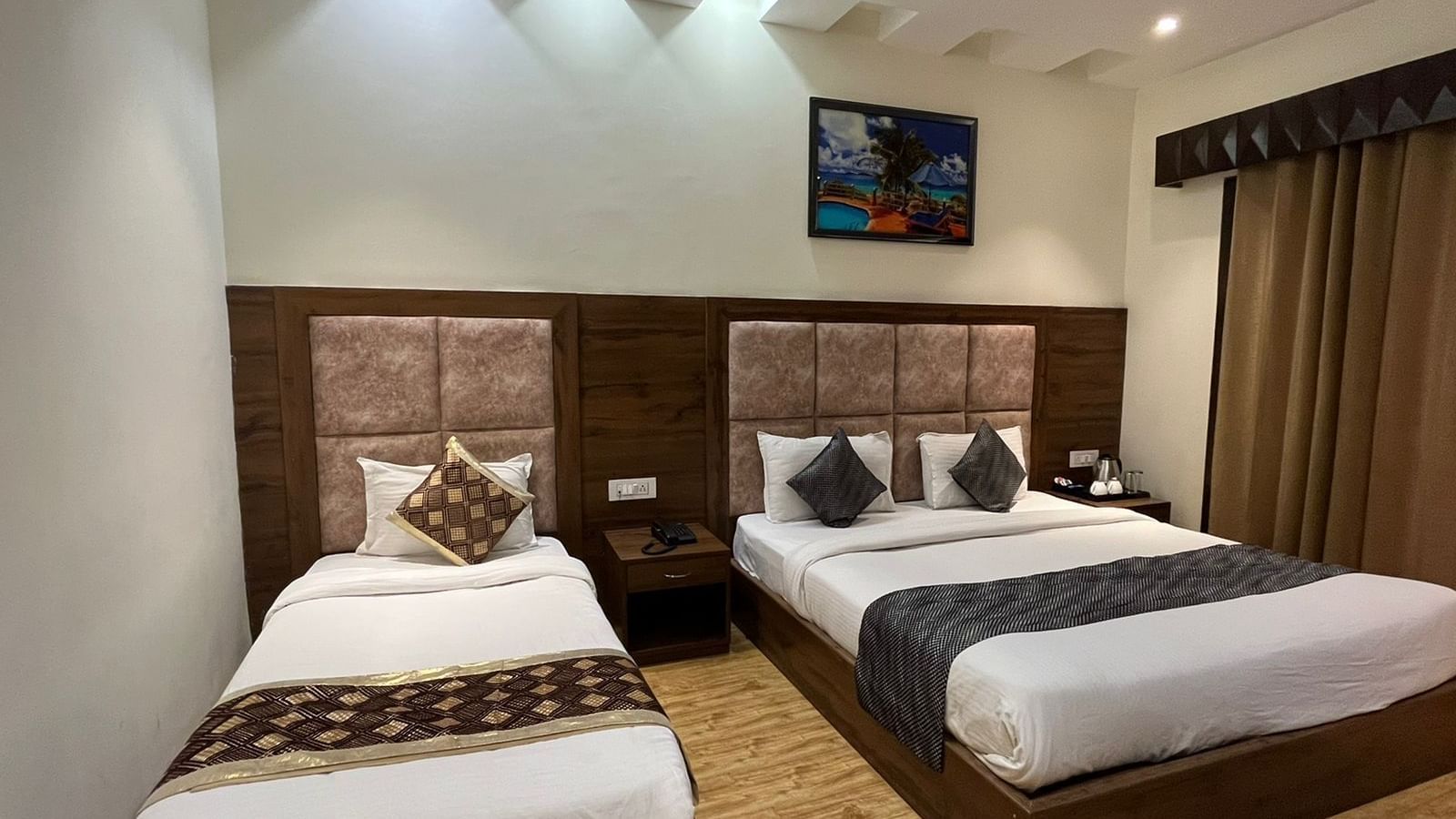 A hotel room with two beds, a queen bed and a single bed, both with matching patterned bedspreads.