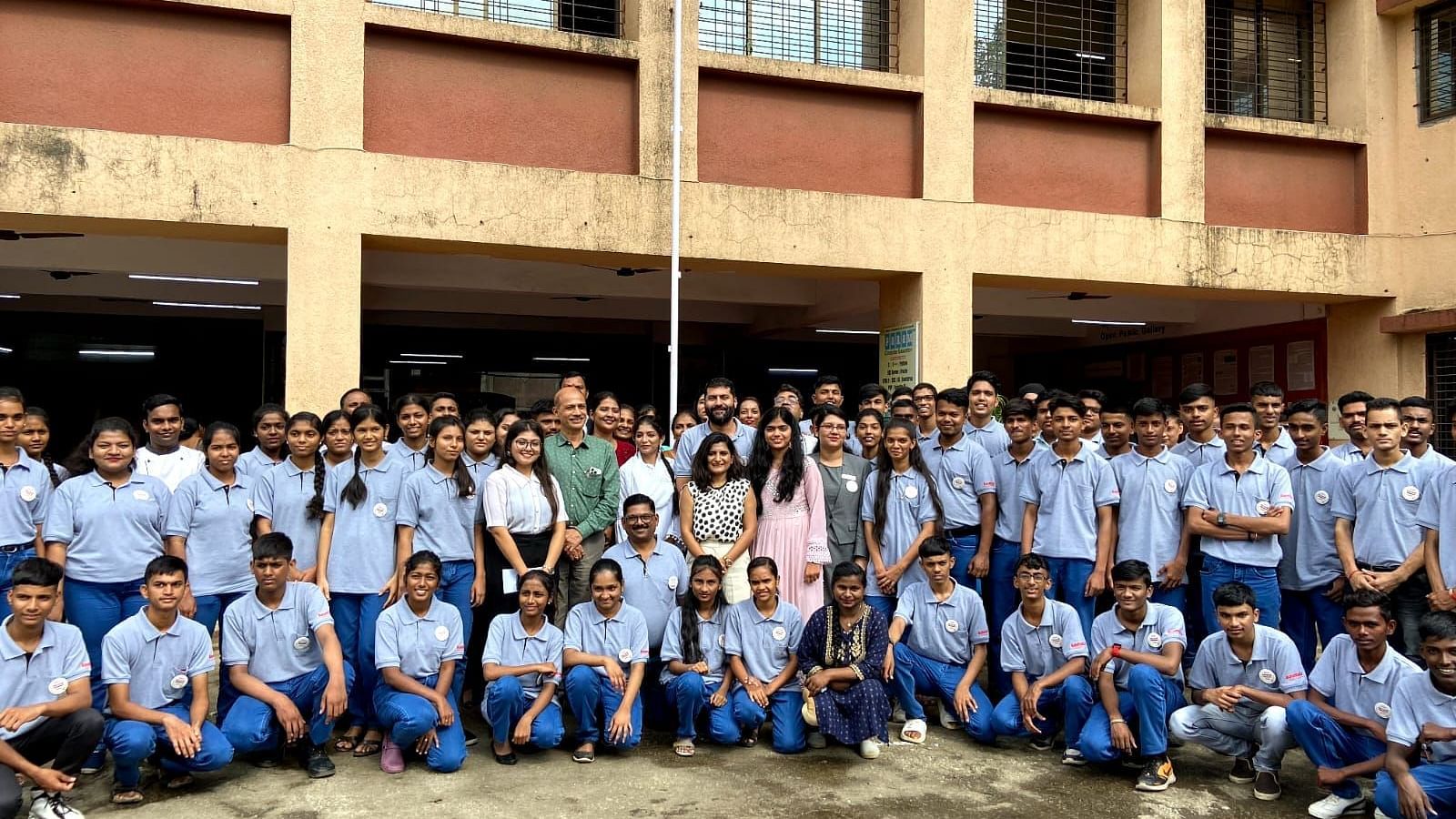 Large group photo with students in blue uniforms outside a college building - Kamats India