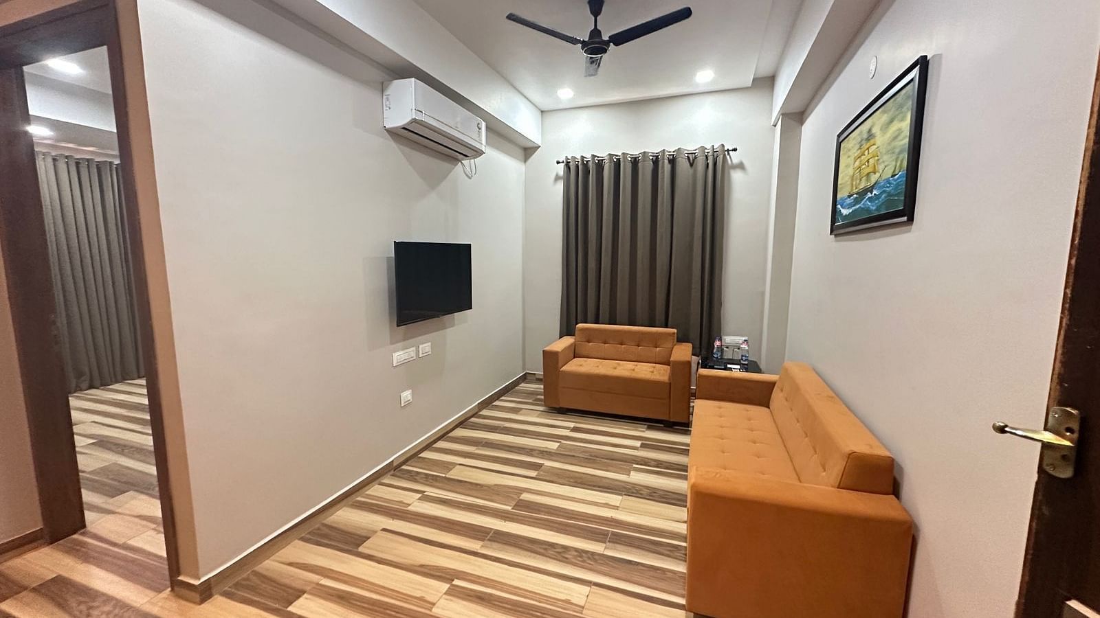 A room features a double bed, a brown sofa, a television, and wooden flooring - Kankidham Lords Inn