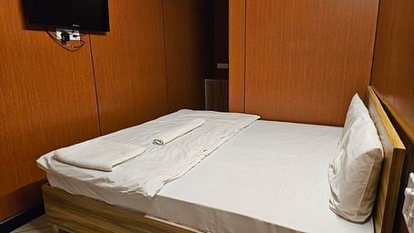 Corner view of a double bed with plain white bed sheet along with a wall mounted television at the Dream Vision Guest House.
