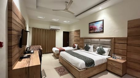 A clean, modern hotel room with a single queen-sized bed, a wooden headboard, and a flatscreen TV mounted on the wall.