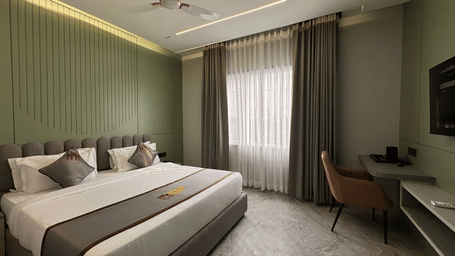 A wide angle shot of the Deluxe Room with ample of natural light coming from the window covered by thin linen curtains, highlighting the bed.