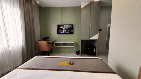 The television, work station, and the minibar of Deluxe Room being overllooked by the double bed kept opposite to them at Hotel Mumbai House, Pithampur.