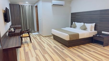 A room at Wild Wings Premium features a double bed with beige and white bedding, dark furniture, and wooden flooring - Kankidham Lords Inn