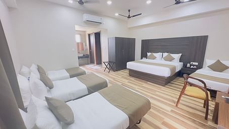 A hotel room contains double beds with white bedding, a single bed, a table, and wooden flooring - Kankidham Lords Inn