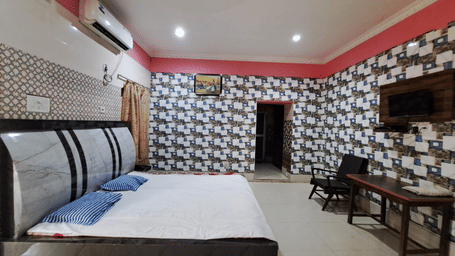 An air conditioner is cooling a Deluxe Room bedroom at Khairi Resorts that is featuring a double bed and a desk.