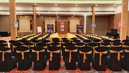 A well-lit and spacious event hall in Lords Eco Inn Shapar Rajkot, featuring neatly arranged chairs and carpeted floor.