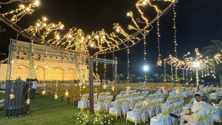 An outdoor venue at night, featuring theatre style seating arrangements, a grand stage backdrop, and string lights at Lords Hrim Akshara Resort Basar with a banquet hall in Basar