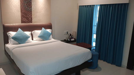A modern hotel room featuring a large bed with white linens, turquoise accent pillows, and dark teal curtains – The Bull Boutique Hotel