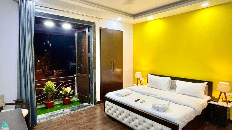Bedroom of Lime Tree Hotels & Service Apartment Private Limited featuring a yellow accent wall, white bedding, and a view of greenery through the window.
