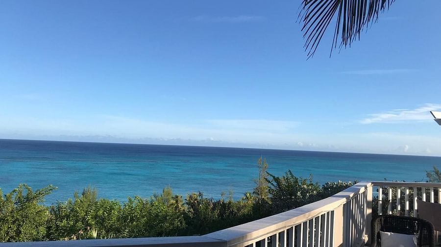 View of the ocean and trees from a deck with a chair and railing | A Stone's Throw Away