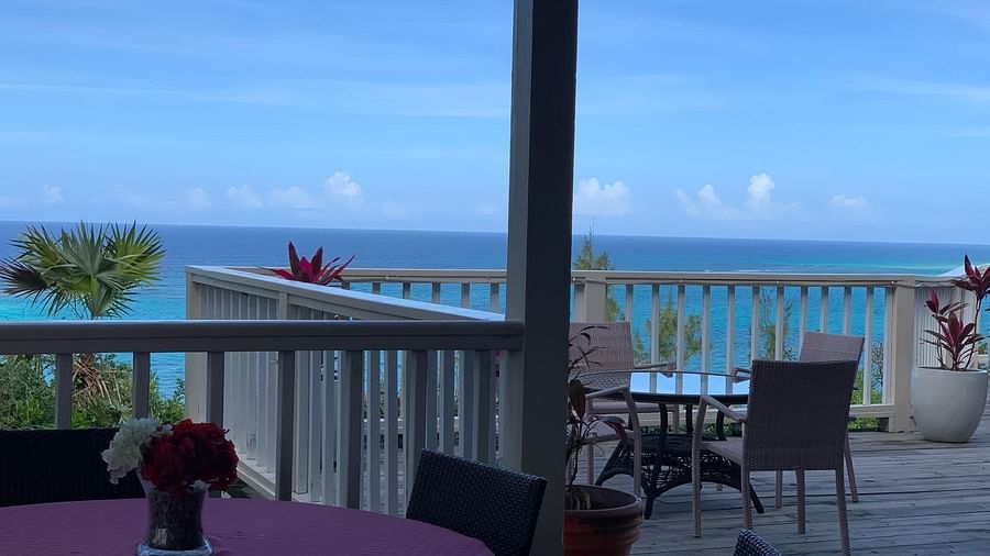 Patio with tables and chairs, flower centerpieces on the tables, and ocean visible beyond railing | A Stone's Throw Away