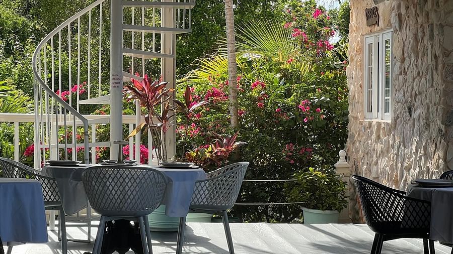 Outdoor dining area with black chairs and spiral staircase surrounded by lush plants | A Stone's Throw Away