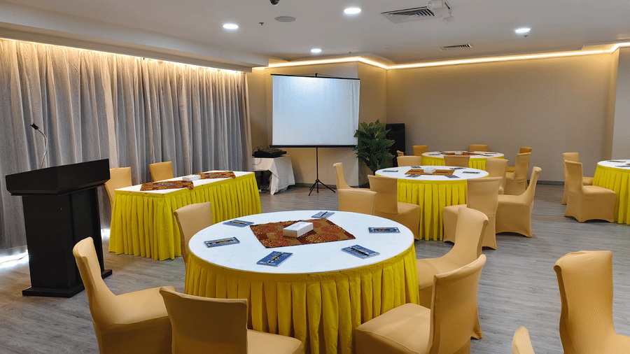 Round banquet tables with yellow cloths and tan chairs are arranged in a multi-purpose hall with a lectern - Al Manar Grand Hotel Apartment, Bur Dubai