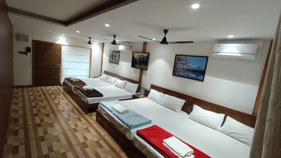 Wide interior of a high-capacity guest room with multiple beds, air conditioning, and wall-mounted televisions - DAN Resorts & Weddings, Palghar