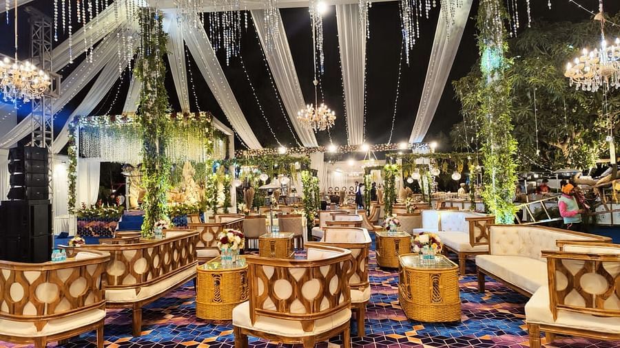 A beautifully decorated outdoor wedding venue with chandeliers, draped fabric, and seating arrangements on a colorful carpet.