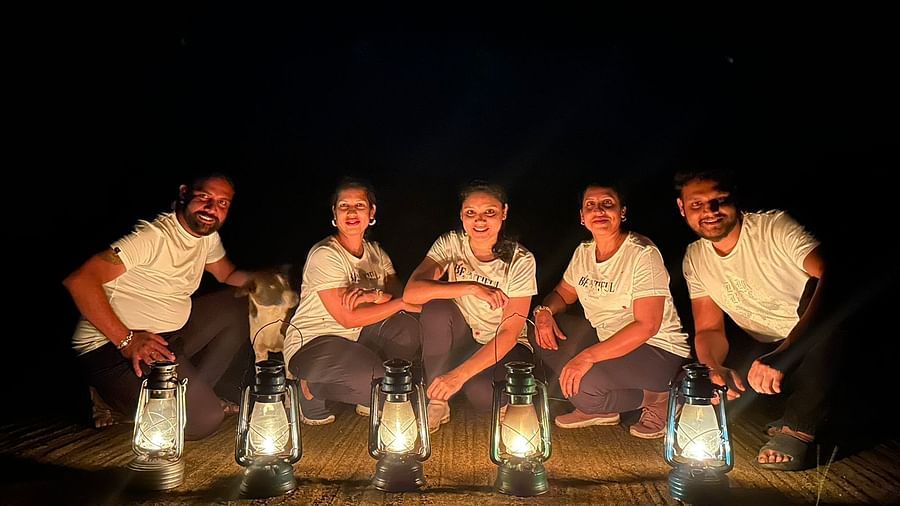 A family sitting around at night, illuminated by lanterns, in a rustic outdoor setting - Evergreen County