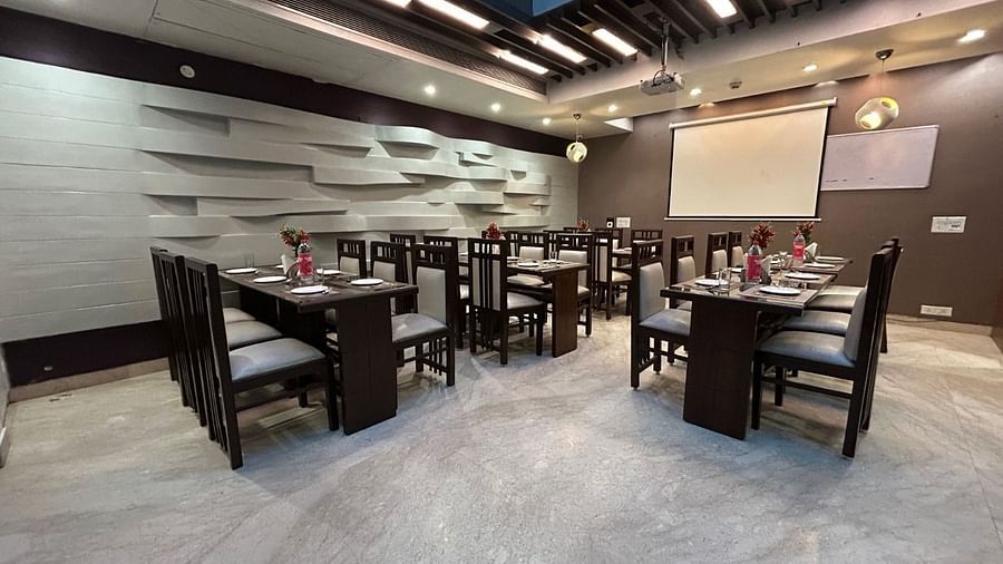A modern dining space with neatly arranged tables and chairs, set against sleek grey walls with stylish ceiling lights - Hotel Emerald, Chandigarh