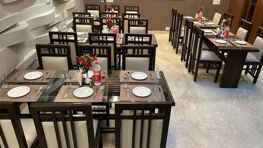A restaurant setup with neatly arranged tables, featuring white plates, red napkins, and a modern ambience - Hotel Emerald, Chandigarh