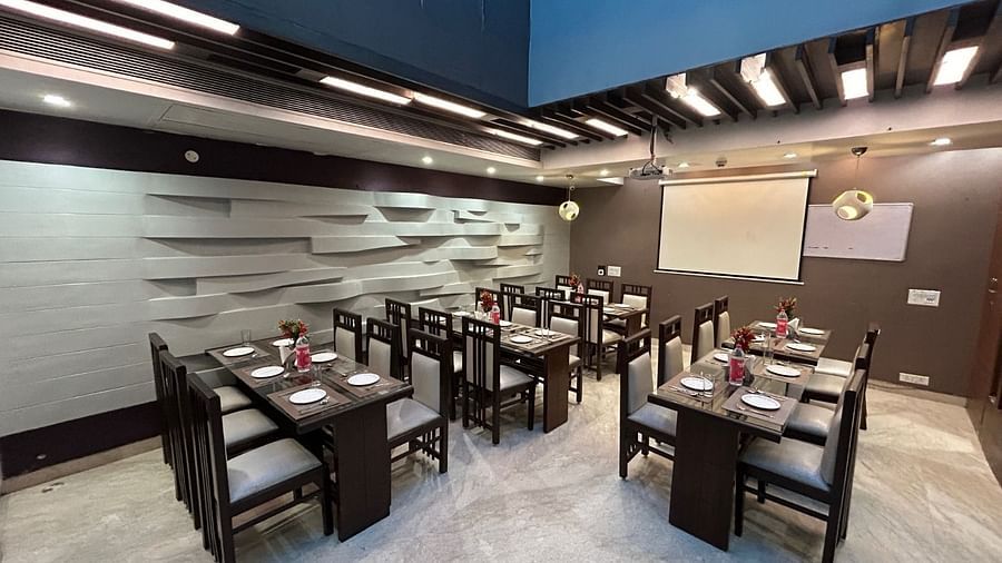 A spacious restaurant with multiple dining tables, a minimalist grey design, and a whiteboard in the background - Hotel Emerald, Chandigarh