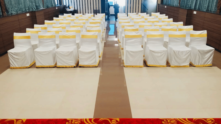 View from the stage looking over theatre style seating arranged with white chair covers inside Gangai Hall at Hotel Grand Sabarees Madurai.