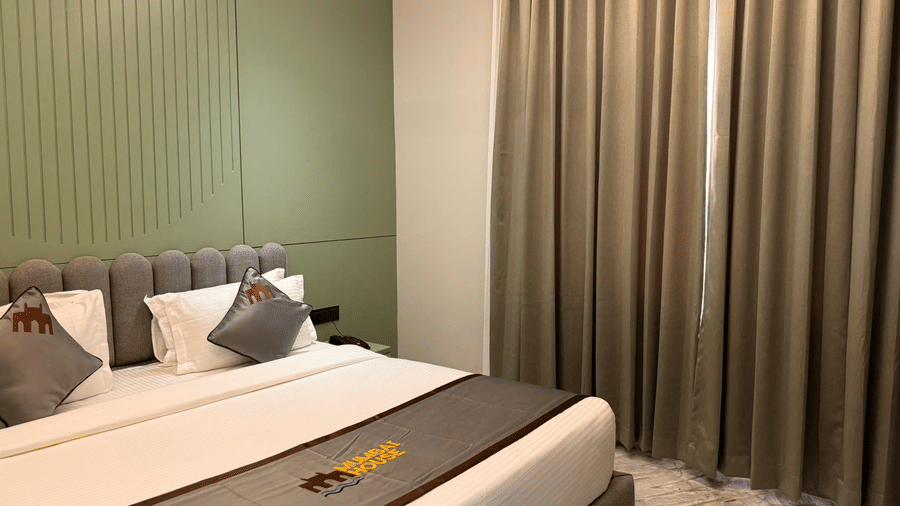 A close-up shot of the corner of the double bed at the Deluxe Room, with grey cushions and a bed runner kept appropriately at Hotel Mumbai House, Pithampur.