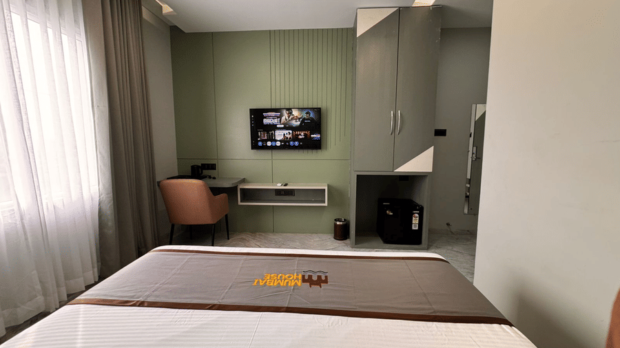 The television, work station, and the minibar of Deluxe Room being overlooked by the double bed kept opposite to them at Hotel Mumbai House, Pithampur.