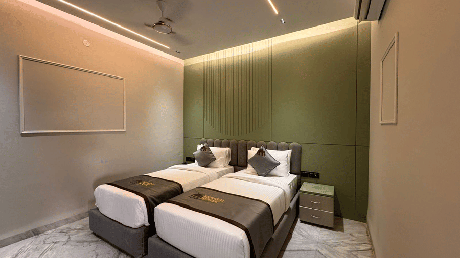 A wide angle shot of the Deluxe Twin Room featuring an olive green master wall and a set of twin beds sharing the wall at Hotel Mumbai House, Pithampur.