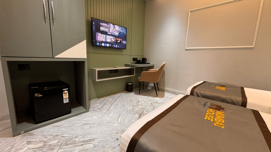 An overview of the Deluxe Twin Room featuring a wall-mounted television with several options for the shows, along side a wardrobe and a mini fridge at Hotel Mumbai House, Pithampur.