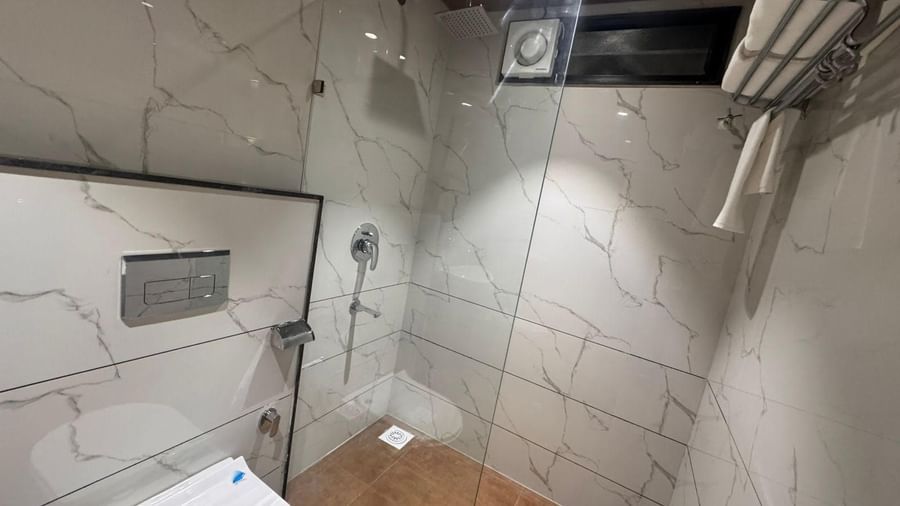 Stylish bathroom at Hotel Mumbai House, Vijay Nagar, Indore, designed with a glass shower enclosure, premium fittings, and marble walls for comfort.
