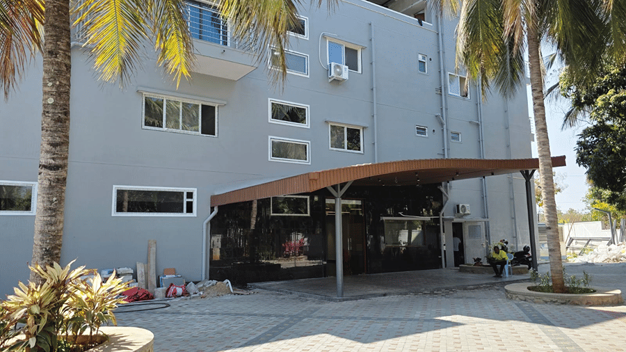Multi-storey hotel exterior with a covered entrance, palm trees, landscaped planters and paved driveway.