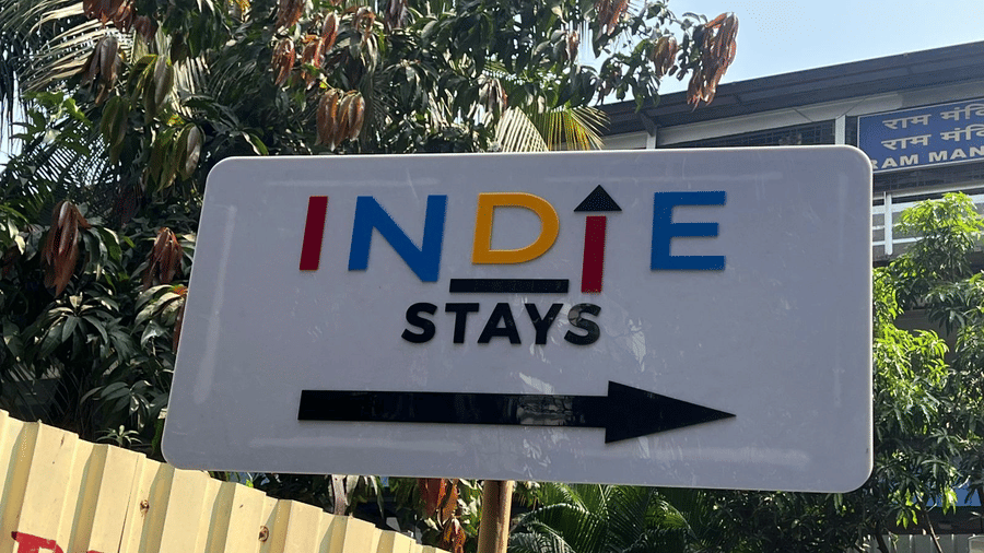 White directional sign with the colourful brand logo pointing toward the entrance of Indie Stays, NESCO Goregaon.