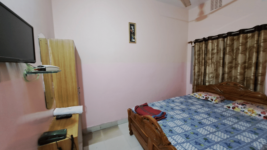 A Standard bedroom at Khairi Resorts displays a double bed, a wooden wardrobe, a TV, and patterned curtains.