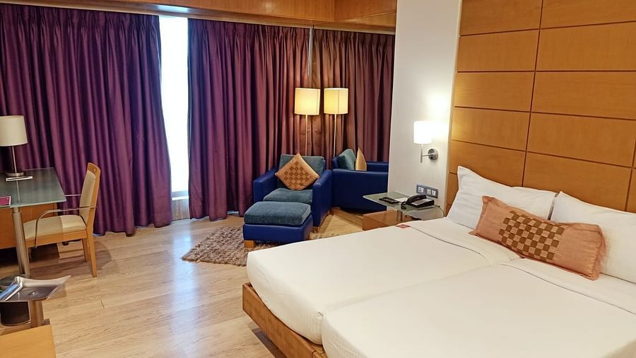 Image of twin beds in the executive twin room at our hotel featuring a flat screen television, bed side table, mirror, violet curtains, and other furniture. | Mirage Hotel
