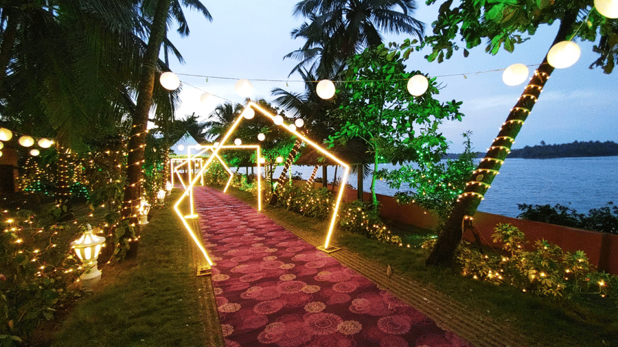 Pathway lined with lights and flowers leading towards the water with palm trees at Paradise Lagoon Resort, Udupi.