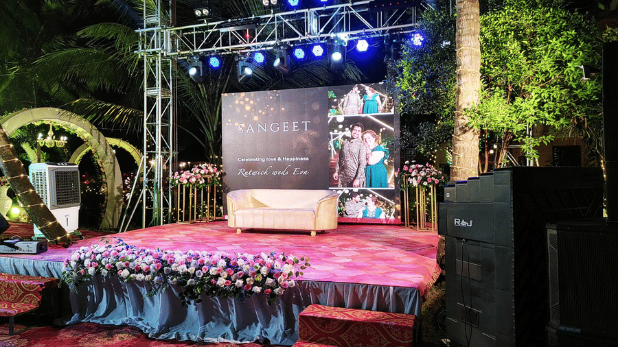 Outdoor stage with floral decorations and LED screen set against palm trees at Paradise Lagoon Resort, Udupi.
