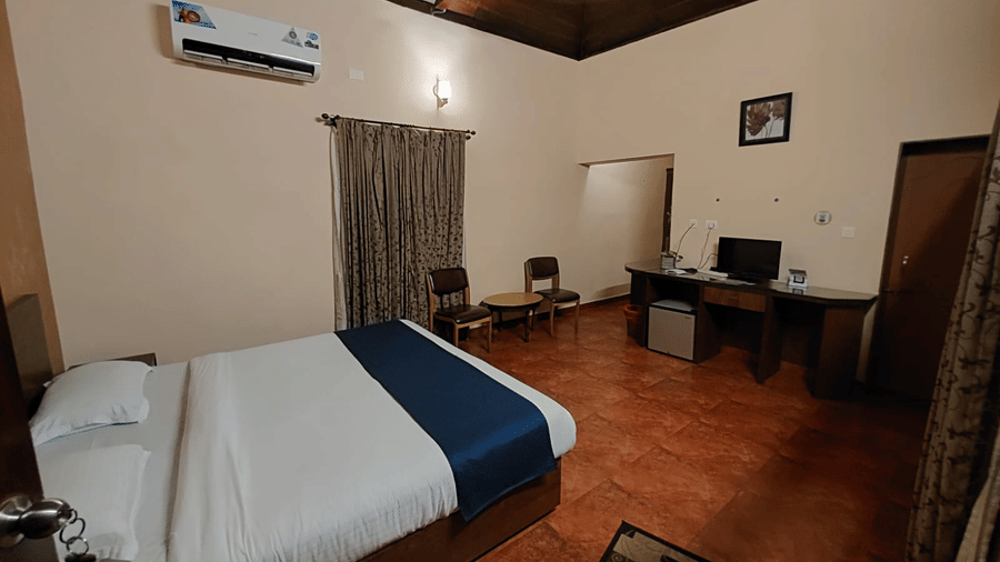 Bedroom with a queen size bed, a round table and wooden chairs, air-conditioning, wall art and a wooden table with television at Paradise Lagoon Resort, Udupi.