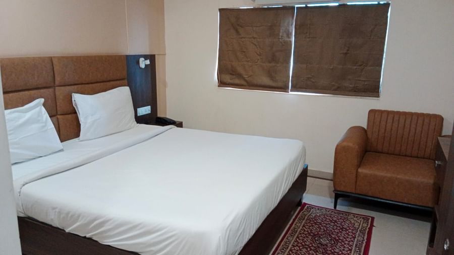 Side view of a double bed at Pravasa Ahmedabad with a brown leather armchair in the corner.