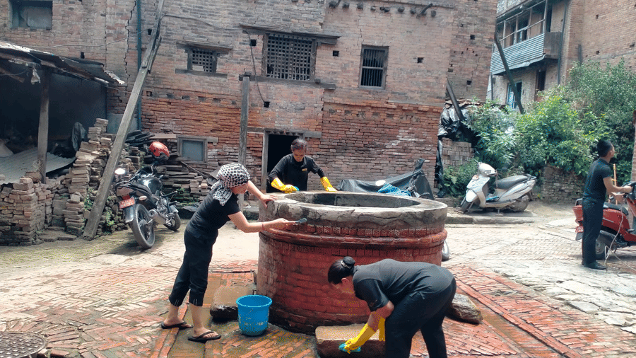 Local residents working together to scrub and clean a traditional stone water well in a brick neighborhood courtyard in Bhaktapur, Nepal.