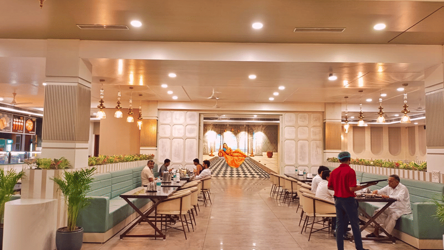A view down the central aisle of the Maharani Ki Rassoii at the Prince ZENQ Xpress Resortt Rohtak, showing light green booth seating on both sides and a few patrons dining.