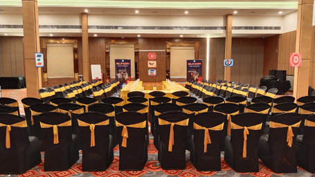 A well-lit and spacious event hall in Lords Eco Inn Shapar Rajkot, featuring neatly arranged chairs and carpeted floor.