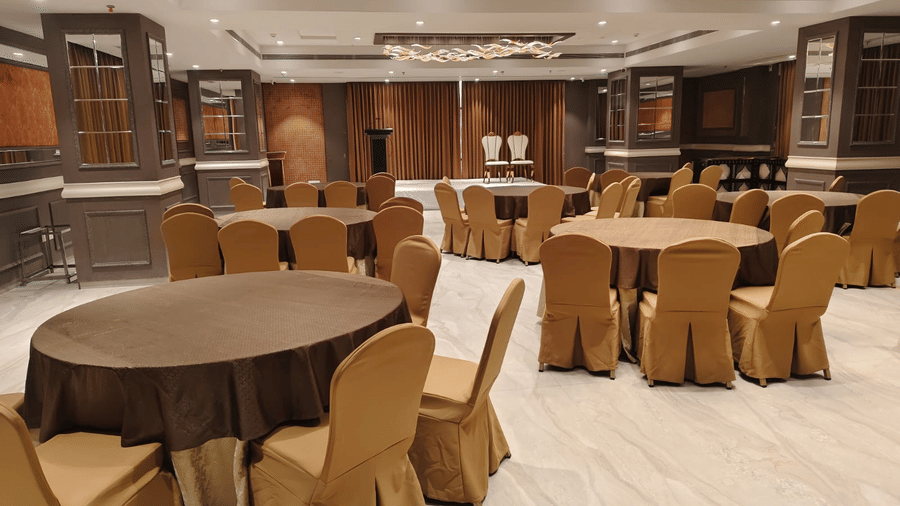 A bright meeting room featuring round tables with gold-coloured chair covers and recessed ceiling lights - Skkylight Lords Inn, Nanded