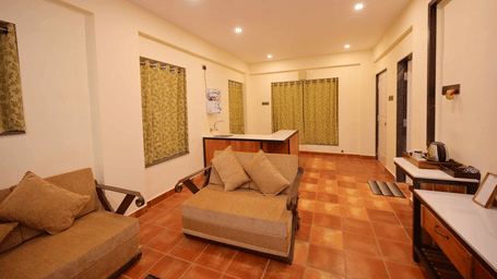 View of a room living area at Agreen Hotels with sofa seating, wooden flooring, green shuttered windows, and warm ambient lighting.