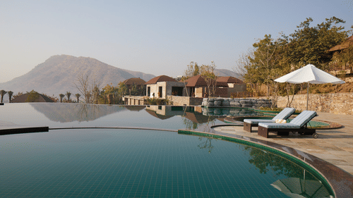 Infinity pool at The Ananta Udaipur which also has lounger beds, and hut style houses nearby.