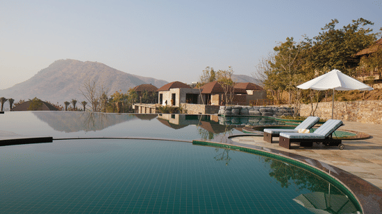 Infinity pool at The Ananta Udaipur which also has lounger beds, and hut style houses nearby.