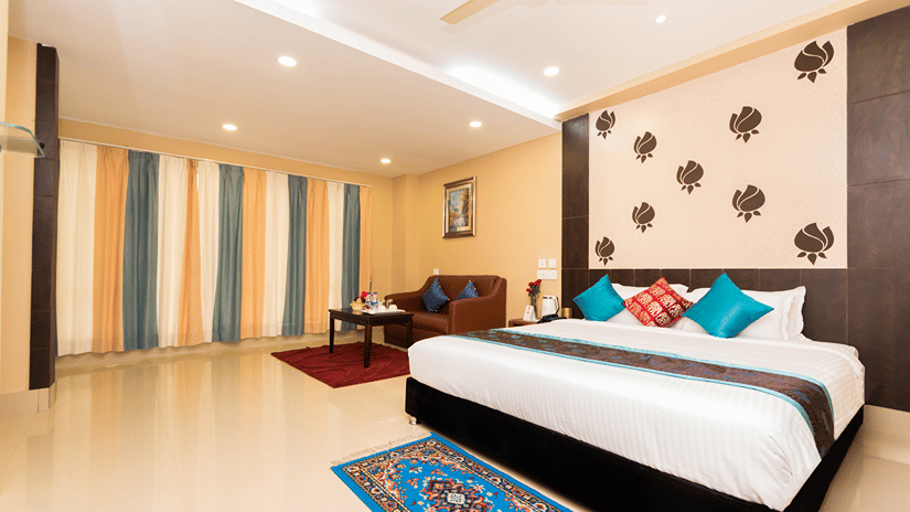 Bedroom of Club King Room at Central Courtyard Boutique Hotel, Siliguri, with bed and a carpet at its foor next to a sitting area