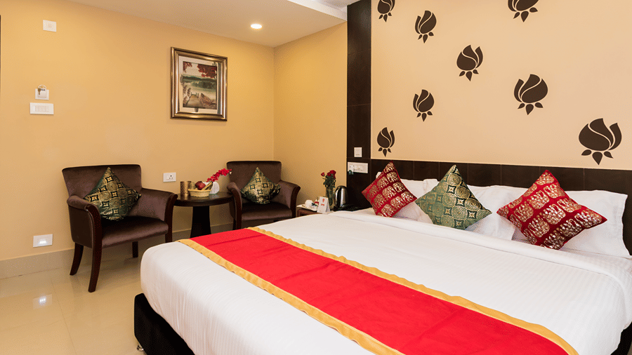 One of the hotel rooms in Siliguri at Central Courtyard Boutique Hotel featuring plush bed against a wall with floral patterns and a seating space for 2 next to it