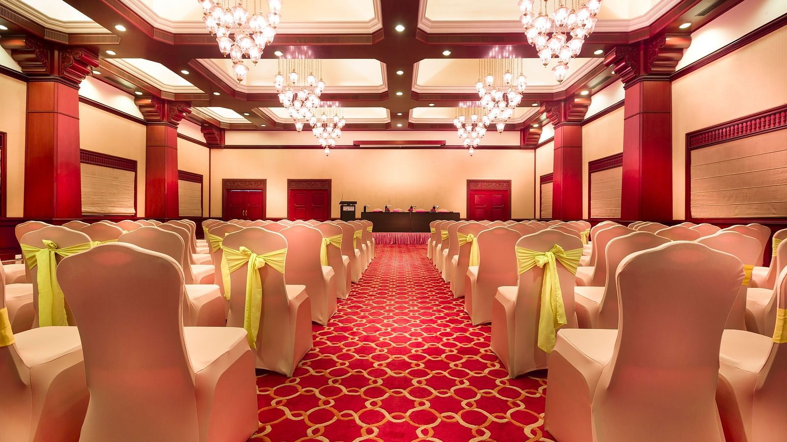 A wedding hall with white chairs tied with yellow ribbons pointing towards the stage at Grand Chennai By GRT Hotels.