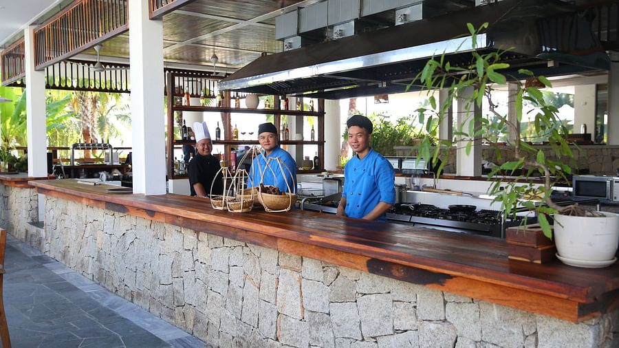 An image of three chefs smiling near the kitchen counter table - Alibu Resort Nha Thrang