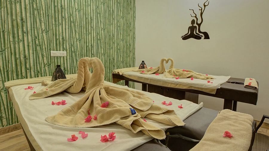 Cosy spa room with two massage tables, folded towels, rose petals, and a bamboo-themed wall. - Bamboo Saa, Udaipur
